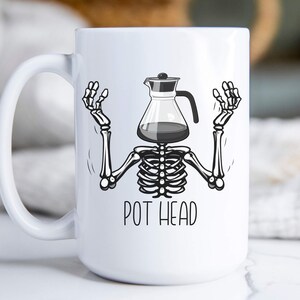 May include: White ceramic coffee mug with a black and white illustration of a skeleton with a coffee pot for a head. The text "POT HEAD" is printed below the illustration.