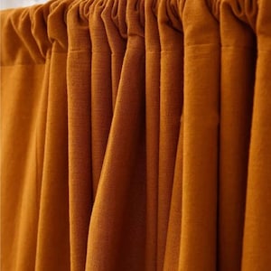 May include: Close-up of a set of mustard-colored curtains. The fabric is textured and hangs in vertical folds, creating a sense of depth. The curtains are attached to a rod at the top, with a gathered header. The color is a warm, earthy tone.