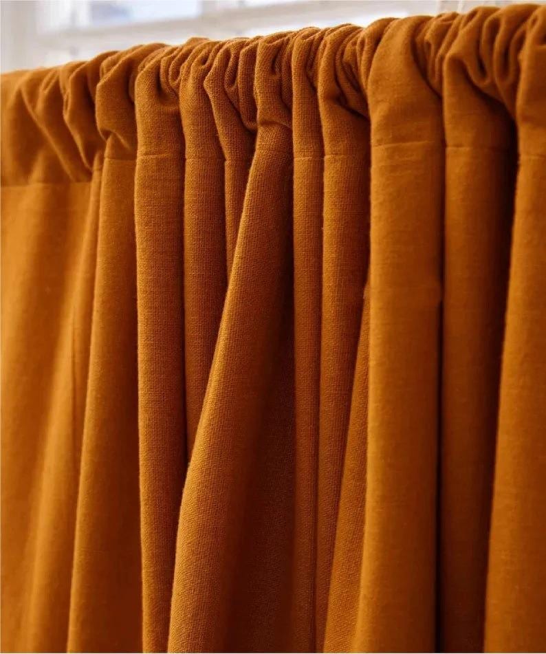 May include: Close-up of a set of mustard-colored curtains. The fabric is textured and hangs in vertical folds, creating a sense of depth. The curtains are attached to a rod at the top, with a gathered header. The color is a warm, earthy tone.