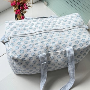 Puede incluir: Una bolsa de viaje blanca y azul con estampado floral y cierre de cremallera. La bolsa tiene dos asas y una correa a rayas. La bolsa est&aacute; hecha de tela acolchada.