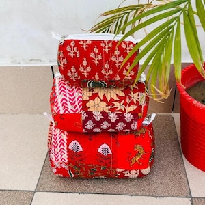 May include: A stack of three rectangular fabric pouches in varying sizes, featuring a vibrant red base color with assorted block-printed patterns including floral motifs, geometric zig-zags, and tiger illustrations, each finished with a white zipper.