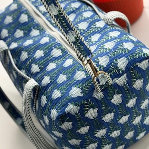 Puede incluir: Bolso de viaje azul con estampado floral blanco. Cuenta con una cremallera blanca y asas a juego. El dise&ntilde;o floral presenta flores blancas y hojas verdes sobre un fondo azul. Las asas son a rayas blancas y azules.
