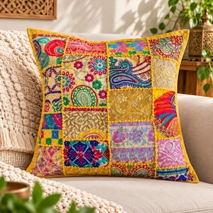 Puede incluir: Un cojín cuadrado con un diseño de patchwork vibrante que presenta varios paneles de tela bordados en tonos amarillo, rosa, azul, verde y dorado. La superficie muestra intrincados patrones florales y de cachemira con costuras decorativas.
