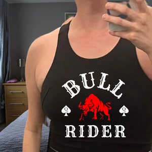 May include: Black tank top with a white graphic of a red bull and the text "BULL RIDER" with two spade symbols.