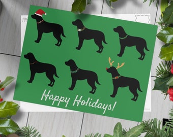 Puede incluir: Una tarjeta de Navidad verde con el texto "¡Felices Fiestas!" y siluetas de seis labradores negros que llevan accesorios festivos. Un perro lleva un gorro de Papá Noel, otro lleva una diadema de reno y cuatro llevan collares de Navidad.