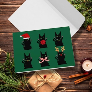 A green card featuring six black cat illustrations. Each cat is in a different holiday outfit. One cat wears a Santa hat, another has a red bow, and a third has a string of lights. The remaining cats are decorated with a green garland, a pink bow, and reindeer antlers.