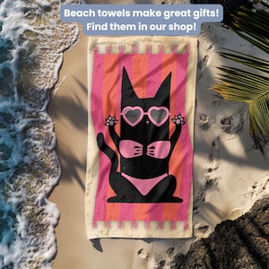 May include: A rectangular beach towel featuring a black cat wearing a pink bikini and heart-shaped sunglasses. The cat is centered on a background of vertical pink and orange stripes with fringed edges at the top and bottom of the towel.
