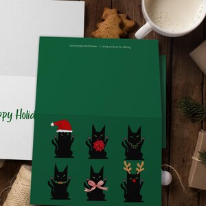 A green card featuring six black cat illustrations. Each cat is in a different holiday outfit. One cat wears a Santa hat, another has a red bow, and a third has a string of lights. The remaining cats are decorated with a green garland, a pink bow, and reindeer antlers.