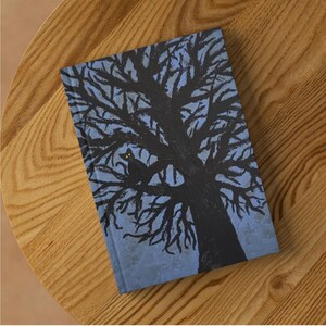 May include: A hardcover book with a dark blue cover featuring a black tree silhouette with an owl perched on a branch. The background is a lighter blue, and the book is on a wooden surface.