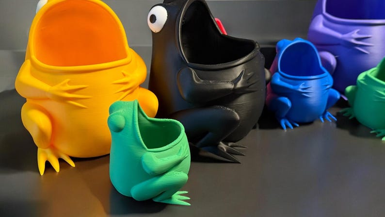 May include: Five frog-shaped planters in different colors, including yellow, black, blue, green, and purple. The planters are all made of plastic and have a wide opening at the top for planting.