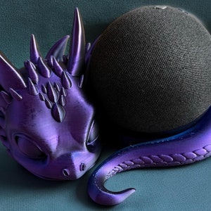 May include: A purple dragon figurine with a textured surface and a black speaker behind it.