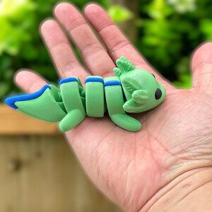 May include: A green and blue segmented axolotl figurine with a cute cartoon face. The figurine is made of plastic and is about 5 inches long.