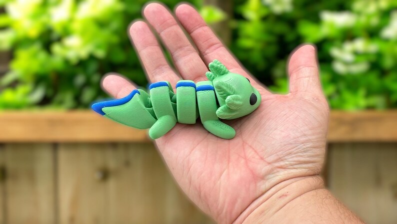 May include: A green and blue segmented axolotl figurine with a cute cartoon face. The figurine is made of plastic and is about 5 inches long.