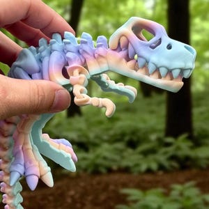 Puede incluir: Un juguete de esqueleto de dinosaurio colorido en tonos pastel de azul, morado y melocot&oacute;n. El juguete se sostiene contra un fondo borroso de bosque. El cr&aacute;neo y los huesos del dinosaurio son claramente visibles.