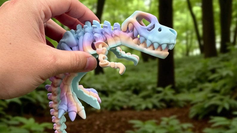 Puede incluir: Un juguete de esqueleto de dinosaurio colorido en tonos pastel de azul, morado y melocot&oacute;n. El juguete se sostiene contra un fondo borroso de bosque. El cr&aacute;neo y los huesos del dinosaurio son claramente visibles.