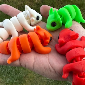 Könnte beinhalten: Vier kleine, bewegliche Spielzeugdrachen aus Plastik. Die Drachen sind in verschiedenen Farben: weiß, orange, grün und rot.