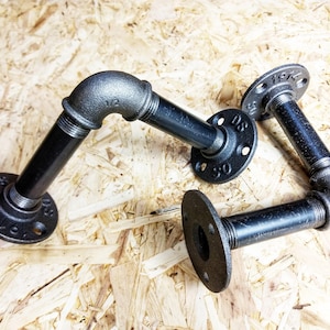 Op de afbeelding: Drie zwarte metalen pijpbeugels met flenzen. De flenzen zijn gemarkeerd met de tekst "1/2" en "3/4".