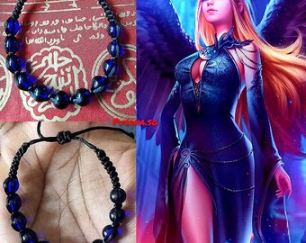 Op de afbeelding: Een zwarte armband van touw met blauwe glazen kralen. De armband is met een knoop vastgemaakt en heeft een kwast aan het uiteinde. De armband zit om een pols.