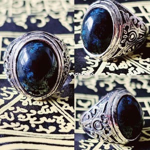 May include: A silver ring with a dark blue oval gemstone set in a decorative band. The ring has intricate details and a vintage style.