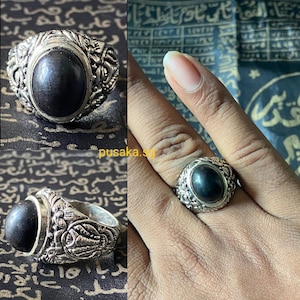 Puede incluir: Un anillo de plata con una piedra ovalada negra engastada en un diseño ornamentado detallado.