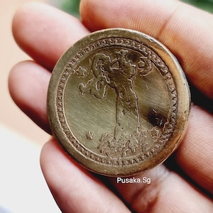 Könnte beinhalten: Nahaufnahme einer runden, goldfarbenen Münze mit einem detaillierten Design, das eine auf einem Sockel stehende Figur zeigt. Die Münze hat einen erhöhten Rand mit einem dekorativen Rand.