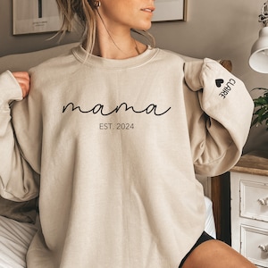 a woman sitting on a bed wearing a sweatshirt