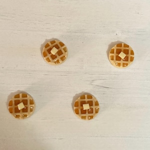 May include: Four miniature waffle cookies with a square of white icing on top. The cookies are arranged in a square pattern on a white surface.