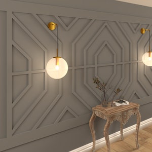 May include: Two gold wall sconces with clear glass globe shades illuminate a room with a geometric patterned wall. A small wooden table with a carved design sits in front of the wall.