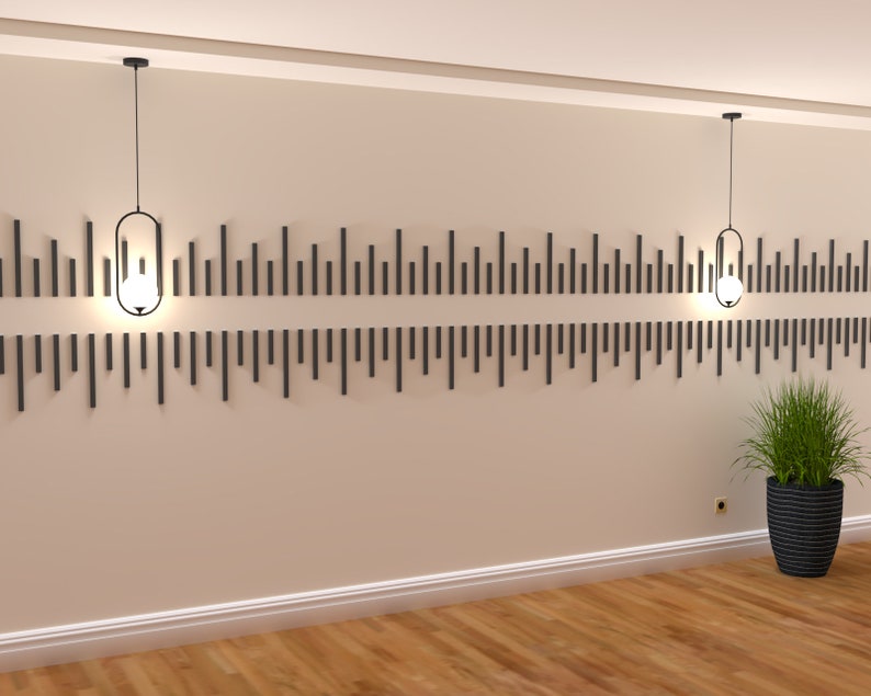 May include: Two black pendant lights with clear glass shades hang from the ceiling in a room with beige walls and a wood floor. A black decorative wall panel with vertical lines is mounted on the wall behind the lights.