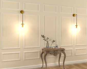 May include: A white wall with gold wall sconces and a small wooden table with a vase of dried branches. The table has a carved design and sits on a wooden floor.