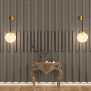 May include: Two gold wall sconces with frosted glass globe shades hang on a gray wall with vertical wood paneling. A small wooden table with ornate legs sits in front of the sconces.