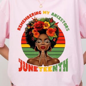 May include: Light pink t-shirt with a graphic on the front and back. The graphic features a woman with a floral headdress, glasses, and praying hands, with the text "Remembering My Ancestors" and "Juneteenth".