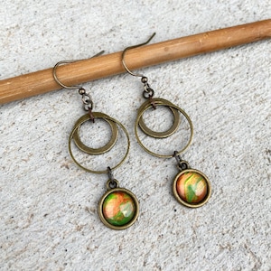 May include: A pair of bronze earrings with a double circle design and a round green, orange, and gold resin pendant.