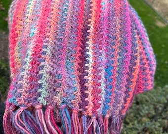 May include: A colorful crocheted scarf with a fringe. The scarf is made with a variety of shades of pink, purple, blue, and green yarn.