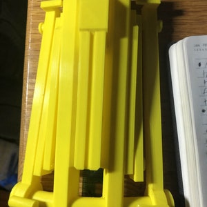 May include: A yellow plastic 3D printed object with multiple interlocking pieces. The object is made up of several flat pieces that are connected together by a series of small, round holes.