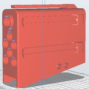 Op de afbeelding: Een 3D-gerenderd, rood rechthoekig object met een handvat aan de bovenkant. Het object heeft verschillende cirkelvormige en ovale gaten aan één kant en twee rechthoekige uitsparingen. Het ontwerp suggereert een mogelijk elektronisch apparaat of behuizing.