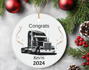 May include: White ceramic Christmas ornament with a black and white semi-truck illustration. The ornament reads "Congrats Kevin 2024".