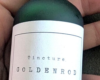 Puede incluir: Una botella de tintura de vidrio verde con un cuentagotas negro. La etiqueta dice "Tincture. GOLDENROD" con instrucciones de dosificación y un volumen de 59 ml. La botella se sostiene en una mano.