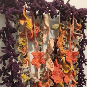 May include: A crocheted wall hanging featuring a variety of autumnal colours, including purple, orange, yellow, and green. The hanging depicts leaves and vines.
