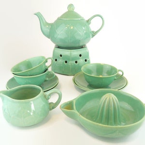 Può includere: Un set da tè in ceramica verde con una teiera, due tazze e piattini, un creamer e uno spremiagrumi. La teiera ha un supporto riscaldante.