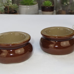 Könnte beinhalten: Zwei kleine braune Keramikschalen mit einer hellbraunen Glasur im Inneren. Die Schalen sind rund und haben einen leicht abgerundeten Boden.