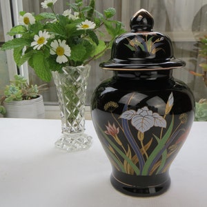 May include: Black ceramic jar with a gold lid and floral design. The jar is decorated with white, blue, green, and gold flowers and leaves.