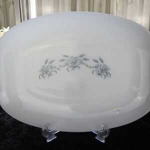 May include: White oval serving platter with a blue and white floral design. The design features a repeating pattern of stylized flowers and wheat stalks.
