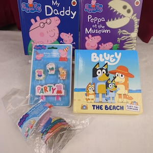 May include: A collection of children's items including a Peppa Pig My Daddy book, a Peppa Pig Peppa at the Museum book, a Bluey The Beach lift-the-flap book, a Peppa Pig birthday candle set in plastic packaging, and a pack of Peppa Pig party hats.