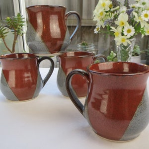 May include: Set of four ceramic mugs with a red and grey glaze. The mugs have a rounded shape and a handle.