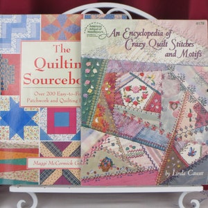 Può includere: Due libri di quilting, uno intitolato "The Quilting Sourcebook" con un design di trapunta patchwork colorato sulla copertina e l'altro intitolato "An Encyclopedia of Crazy Quilt Stitches and Motifs" con un primo piano di una trapunta pazza colorata.