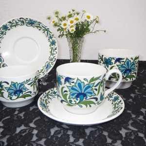 Op de afbeelding: Een set van vier vintage theekopjes en schoteltjes met een blauw en groen bloemenpatroon. De kopjes en schoteltjes zijn wit met een blauw en groen bloemenpatroon. De kopjes zijn allemaal even groot en hebben dezelfde vorm. De schoteltjes zijn allemaal even groot en hebben dezelfde vorm.
