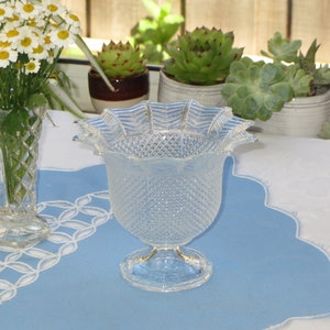 May include: A clear glass vase with a scalloped rim and a diamond pattern. The vase is sitting on a blue and white table runner.