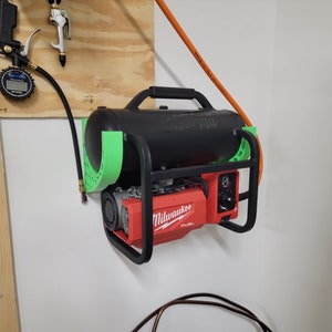 May include: A black air compressor with a red Milwaukee FUEL motor, mounted on a wall. The compressor has a black tank, green supports, and a handle. An air hose and gauge are also visible.