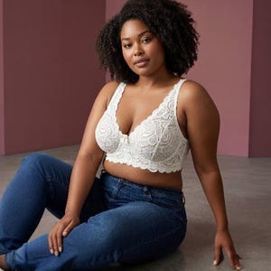 以下が含まれることがあります： スカラップエッジ、深いVネック、中央に小さなリボンのディテールが施された白いレースのブラレットと、ダークブルーのデニムジーンズ。ブラレットには幅広のレースストラップが付いており、バストラインのすぐ下まで届くロングラインのシルエットです。
